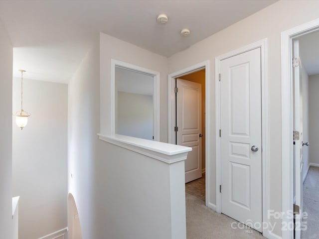 corridor featuring an upstairs landing, baseboards, and light carpet