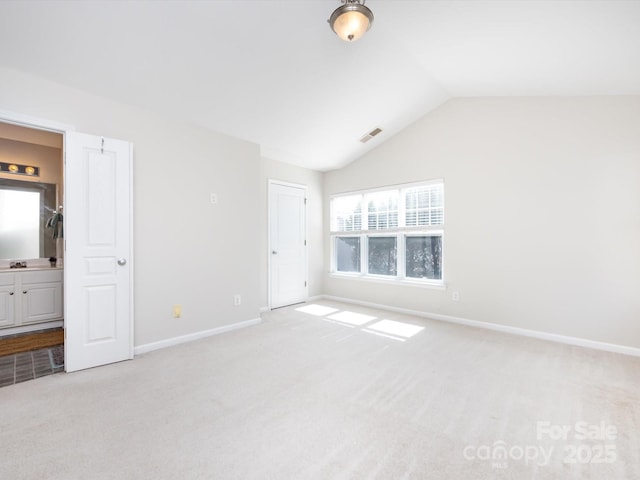 unfurnished bedroom featuring visible vents, lofted ceiling, connected bathroom, baseboards, and light colored carpet