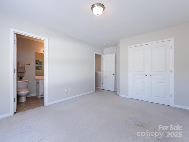 unfurnished bedroom featuring a closet, baseboards, light colored carpet, and ensuite bathroom