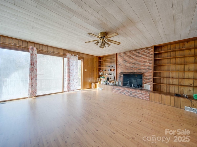 unfurnished living room featuring wood-type flooring, built in features, a fireplace, and wood walls