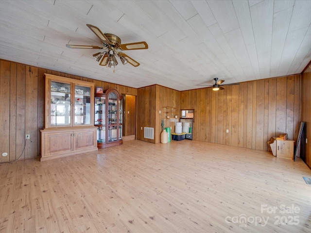 unfurnished living room with ceiling fan, wood walls, and light wood-type flooring