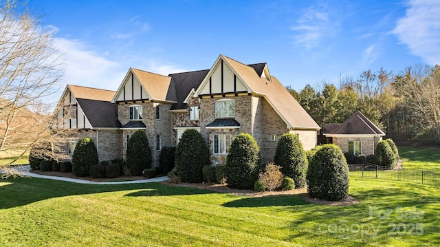 view of side of property featuring a yard, roof with shingles, stone siding, and fence