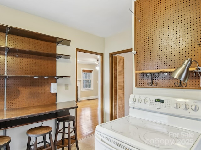 kitchen featuring light hardwood / wood-style flooring, a breakfast bar area, ceiling fan, and electric stove