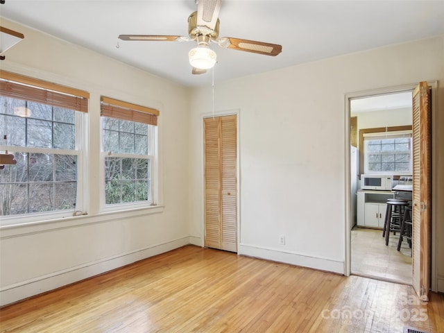 unfurnished bedroom featuring multiple windows, ceiling fan, light wood-type flooring, and a closet