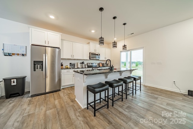 kitchen with stainless steel appliances, an island with sink, white cabinets, and a kitchen breakfast bar