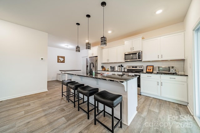 kitchen featuring appliances with stainless steel finishes, white cabinetry, hanging light fixtures, tasteful backsplash, and a center island with sink