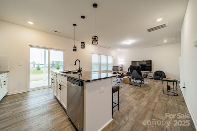 kitchen with a kitchen bar, sink, white cabinetry, stainless steel dishwasher, and an island with sink