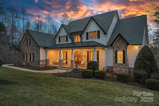 exterior space with stone siding, metal roof, covered porch, a standing seam roof, and a yard