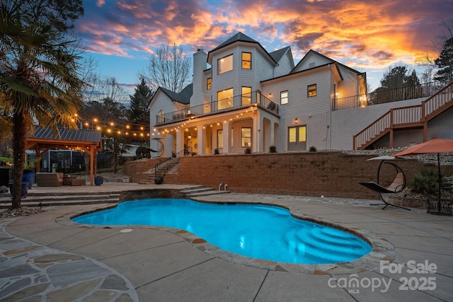 pool at dusk featuring stairway, a patio area, and an outdoor pool