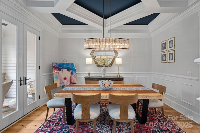 dining area with french doors, a notable chandelier, light wood finished floors, a decorative wall, and coffered ceiling