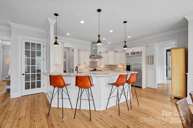 kitchen featuring stainless steel appliances, a breakfast bar, a peninsula, and wall chimney exhaust hood