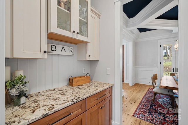 kitchen featuring light stone counters, ornamental molding, light wood finished floors, beamed ceiling, and glass insert cabinets