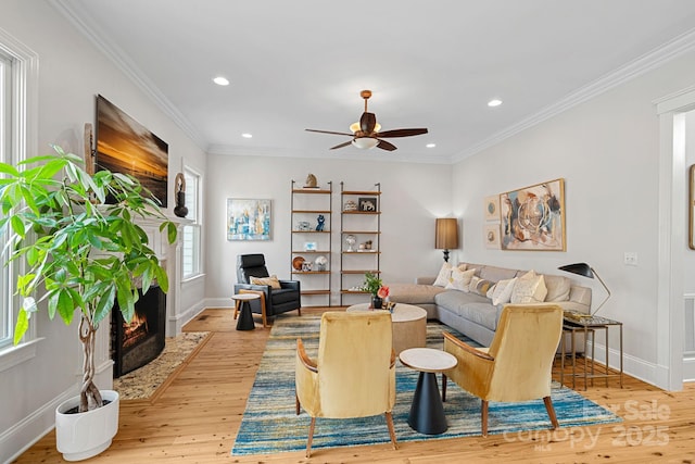 living area featuring crown molding, a fireplace with flush hearth, hardwood / wood-style flooring, and baseboards