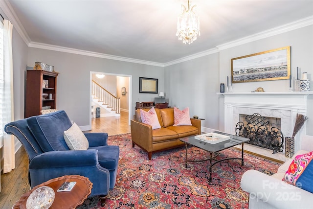 living room with hardwood / wood-style flooring, ornamental molding, a chandelier, and a high end fireplace