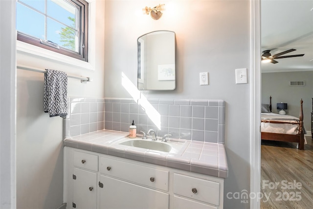 bathroom with ceiling fan, vanity, wood-type flooring, and decorative backsplash