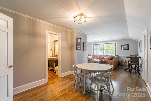 dining room with hardwood / wood-style flooring, ornamental molding, and vaulted ceiling