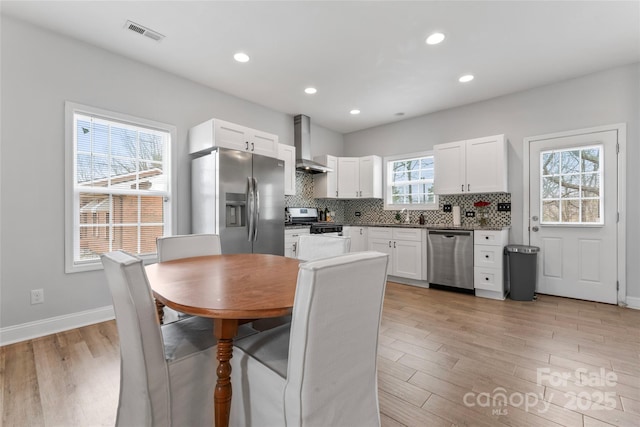 kitchen featuring stainless steel appliances, wall chimney exhaust hood, visible vents, and white cabinets