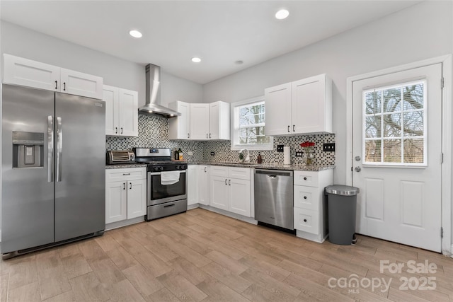 kitchen featuring white cabinets, wall chimney range hood, stainless steel appliances, and dark stone countertops