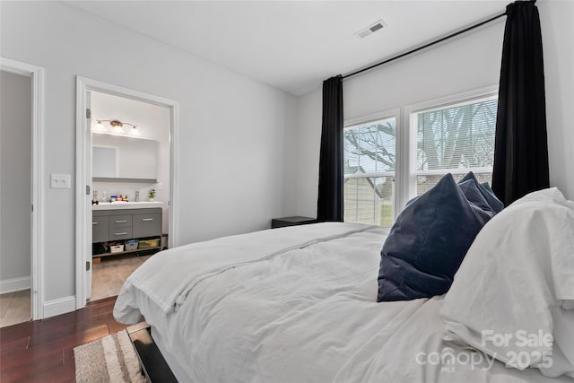 bedroom with dark wood-style floors, baseboards, visible vents, and ensuite bathroom