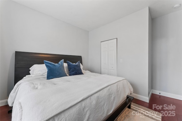 bedroom with a closet, dark wood-style flooring, and baseboards