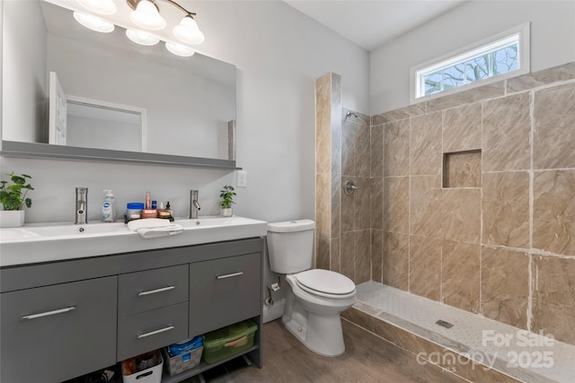 full bathroom featuring a tile shower, double vanity, a sink, and toilet