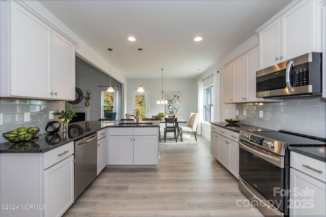 kitchen featuring pendant lighting, white cabinetry, kitchen peninsula, stainless steel appliances, and light hardwood / wood-style flooring