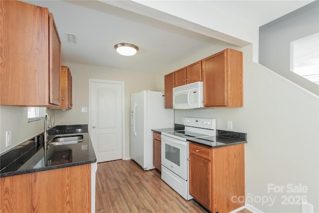 kitchen with sink, dark stone countertops, white appliances, and light hardwood / wood-style flooring