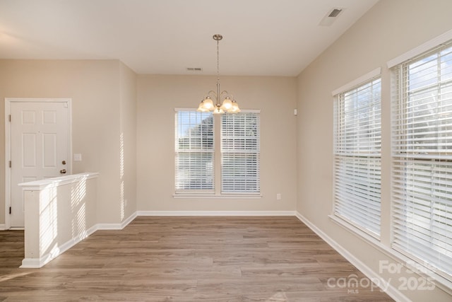 unfurnished dining area with a healthy amount of sunlight, wood-type flooring, and a chandelier