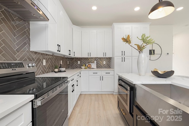 kitchen featuring electric stove, light stone countertops, white cabinets, decorative light fixtures, and wall chimney exhaust hood