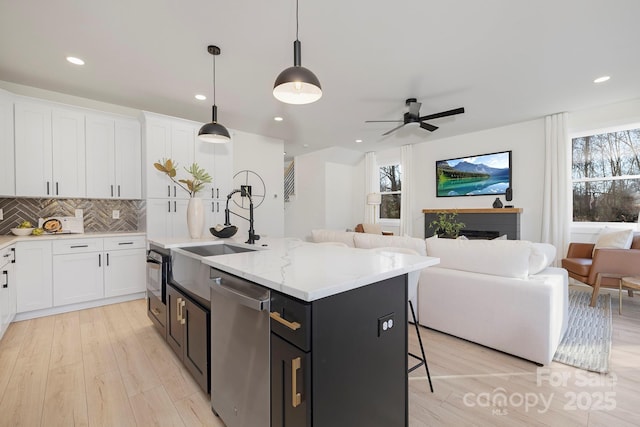 kitchen with dishwasher, an island with sink, sink, white cabinets, and hanging light fixtures