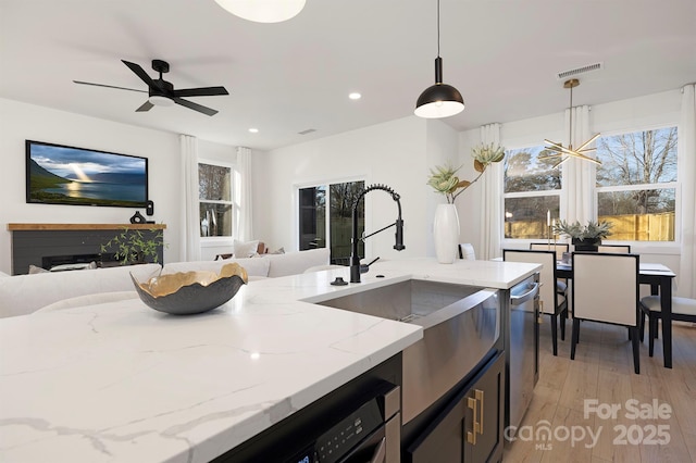 kitchen with pendant lighting, sink, light stone counters, light hardwood / wood-style floors, and stainless steel dishwasher