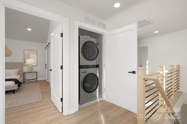 laundry room with a barn door, stacked washer and clothes dryer, and light hardwood / wood-style floors