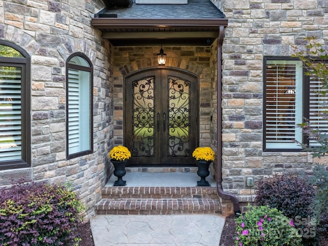 doorway to property with stone siding, roof with shingles, and french doors