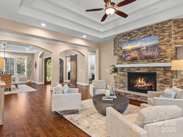 living room with dark wood-style floors, crown molding, arched walkways, and a tray ceiling