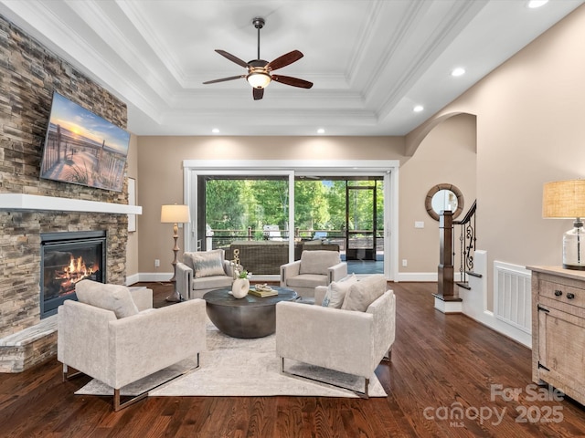 living room with a fireplace, dark hardwood / wood-style flooring, ornamental molding, ceiling fan, and a tray ceiling