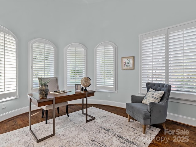 office space featuring baseboards, wood finished floors, visible vents, and a healthy amount of sunlight