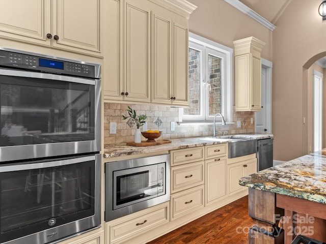 kitchen with dark wood-type flooring, sink, light stone counters, stainless steel appliances, and cream cabinetry