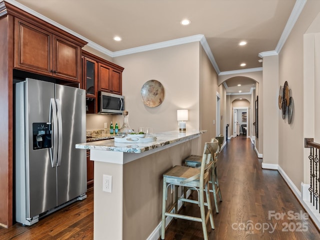 kitchen featuring a breakfast bar, arched walkways, stainless steel appliances, and dark wood-style flooring