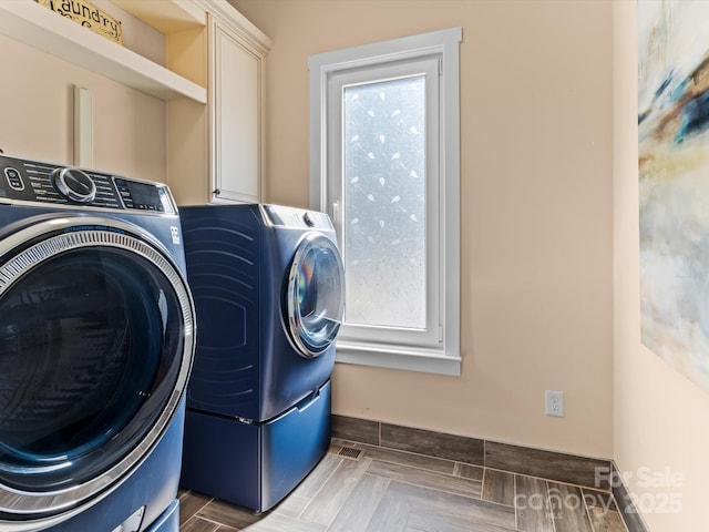 clothes washing area with plenty of natural light, washing machine and dryer, cabinets, and light parquet flooring