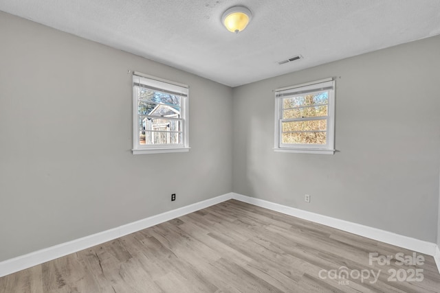 spare room featuring light hardwood / wood-style flooring, a wealth of natural light, and a textured ceiling