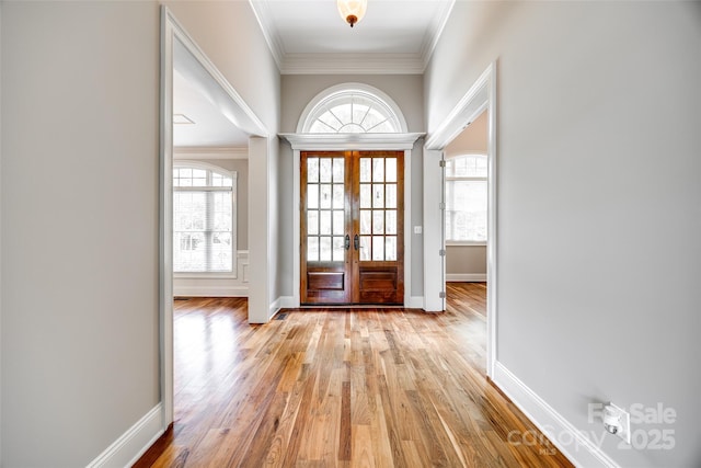 entrance foyer featuring light wood-style floors, plenty of natural light, ornamental molding, and french doors