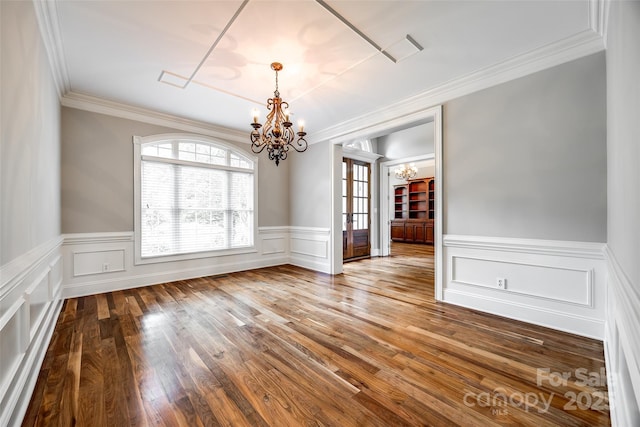 unfurnished dining area featuring a chandelier, ornamental molding, a wainscoted wall, and wood finished floors