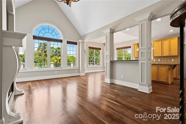 unfurnished living room with dark wood-style flooring, a notable chandelier, decorative columns, and baseboards