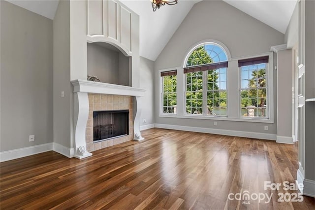 unfurnished living room with high vaulted ceiling, a fireplace, baseboards, and wood finished floors