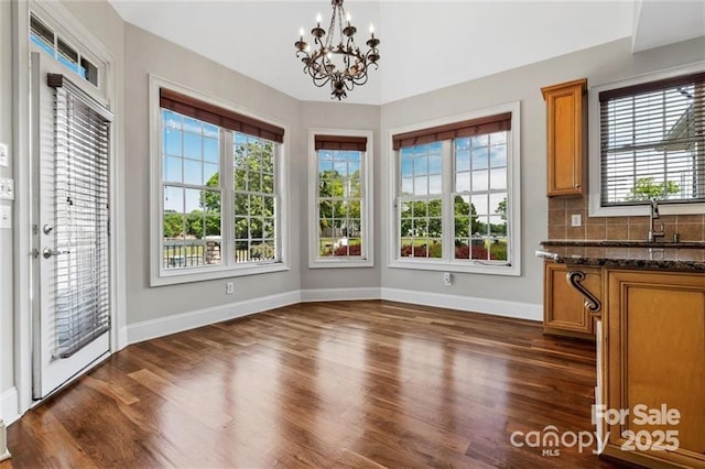 unfurnished dining area with a chandelier, a sink, dark wood finished floors, and baseboards