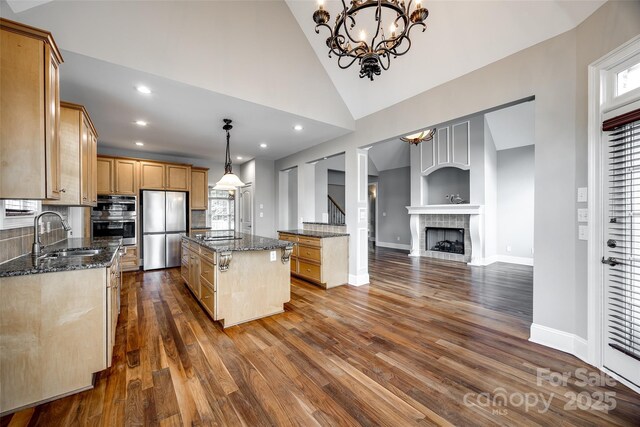 kitchen with appliances with stainless steel finishes, dark stone countertops, dark wood-style flooring, a center island, and a sink