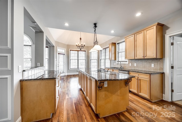 kitchen featuring dark stone counters, a kitchen island, wood finished floors, a sink, and backsplash