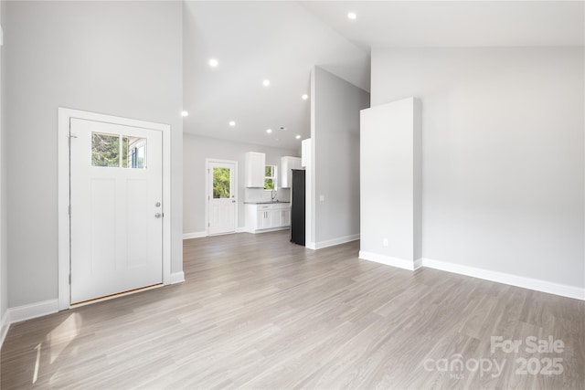 unfurnished living room featuring high vaulted ceiling and light wood-type flooring