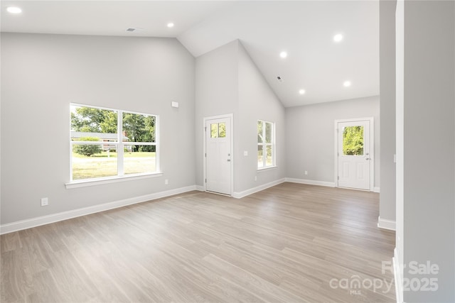 unfurnished living room featuring high vaulted ceiling, a healthy amount of sunlight, and light wood-type flooring