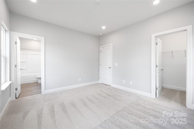 unfurnished bedroom featuring a walk in closet, connected bathroom, a closet, and light carpet